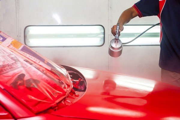 car being red paint sprayed with spray gun in painting booth