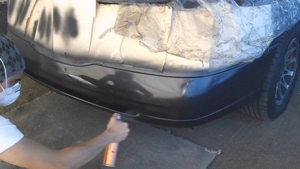 man painting rear end of a car with a spray can