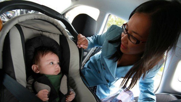 A woman looking over a baby inside a car