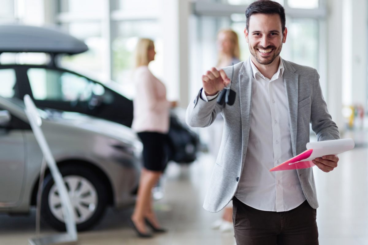 car salesman with a key and a couple in the background