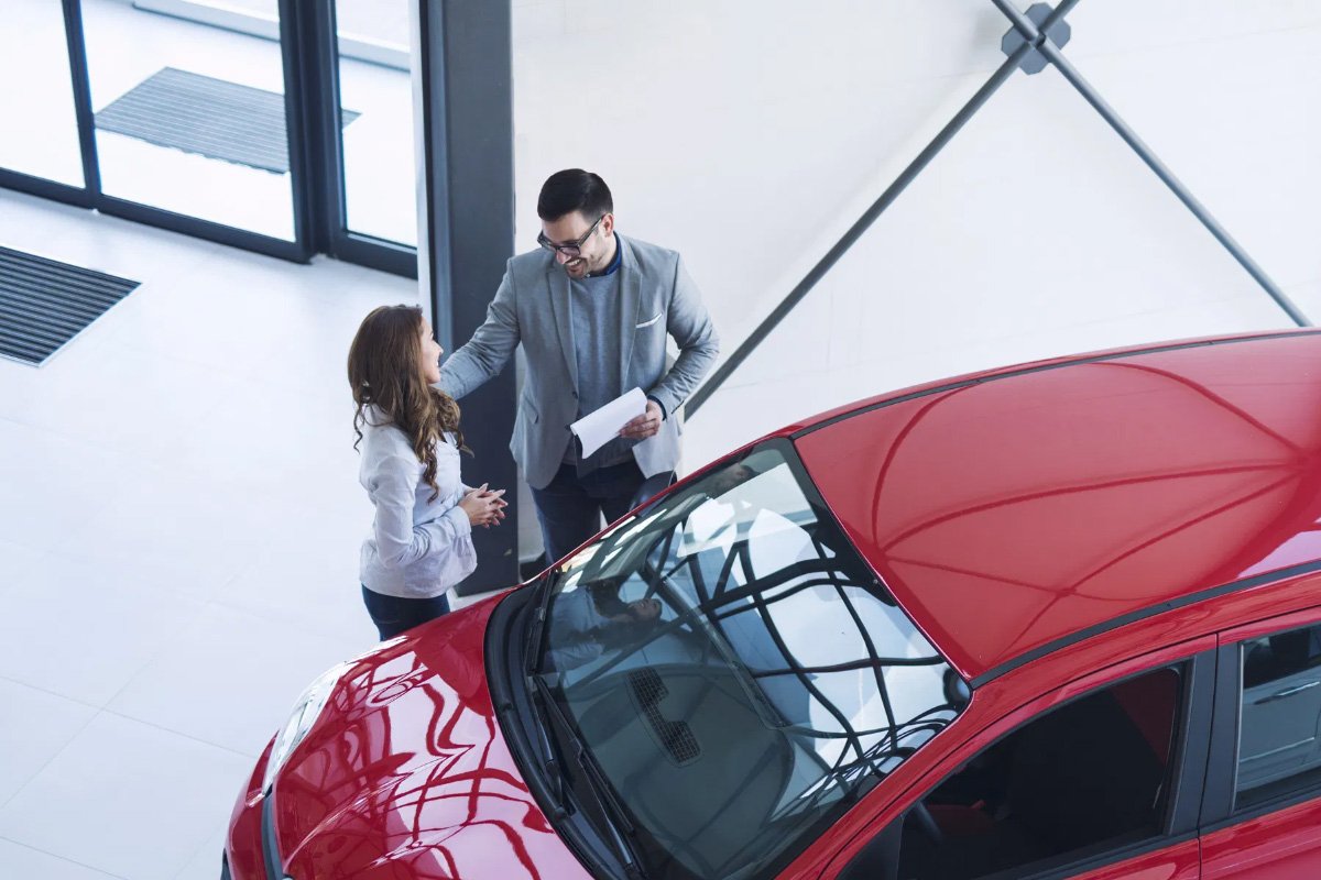 salesman and customer standing next to a red car