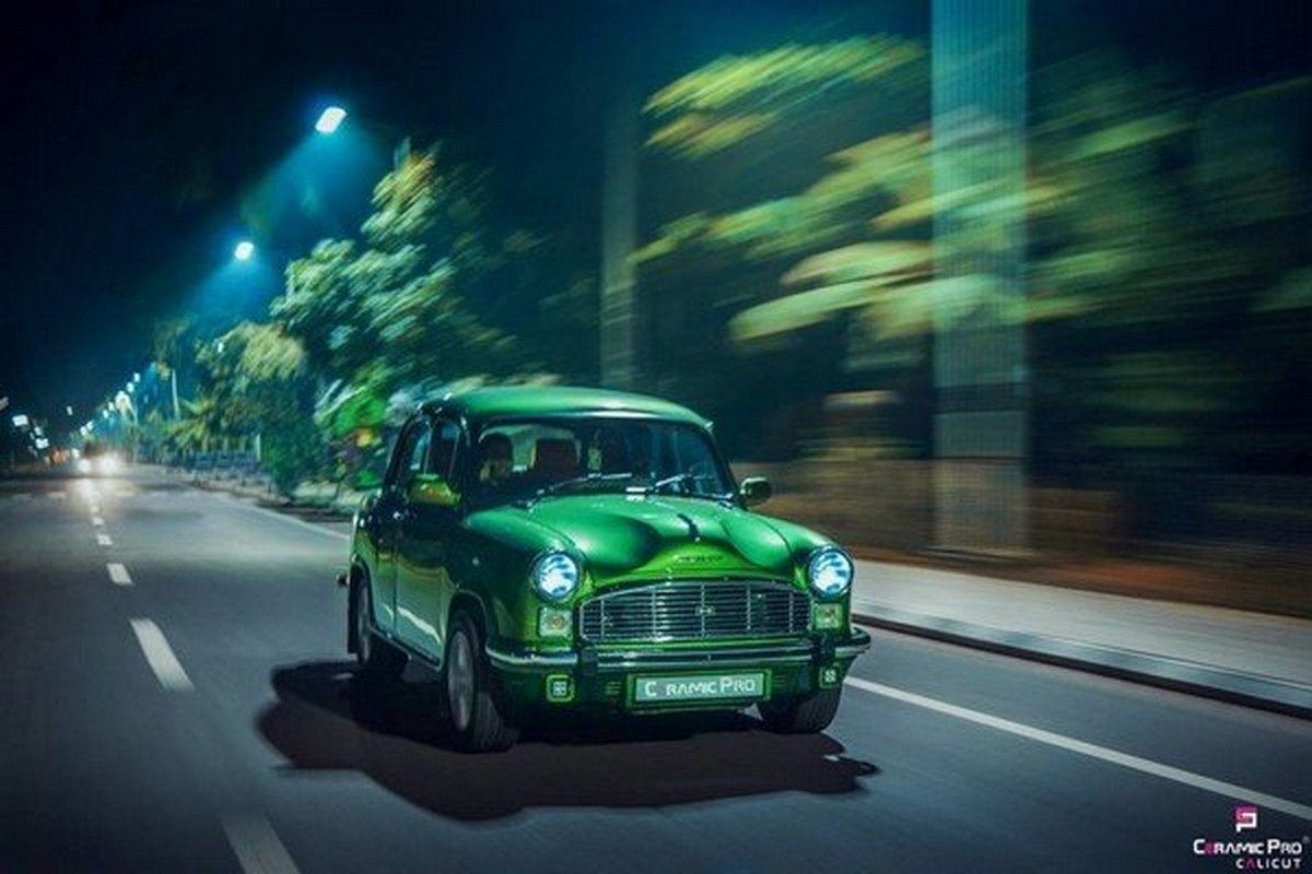 Hindustan Ambassador running on road with headlights with trees background