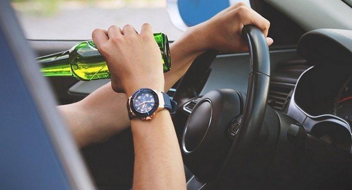 driver drinking while operating vehicle, one human hand holding alcohol bottle, the other holding the steering wheel
