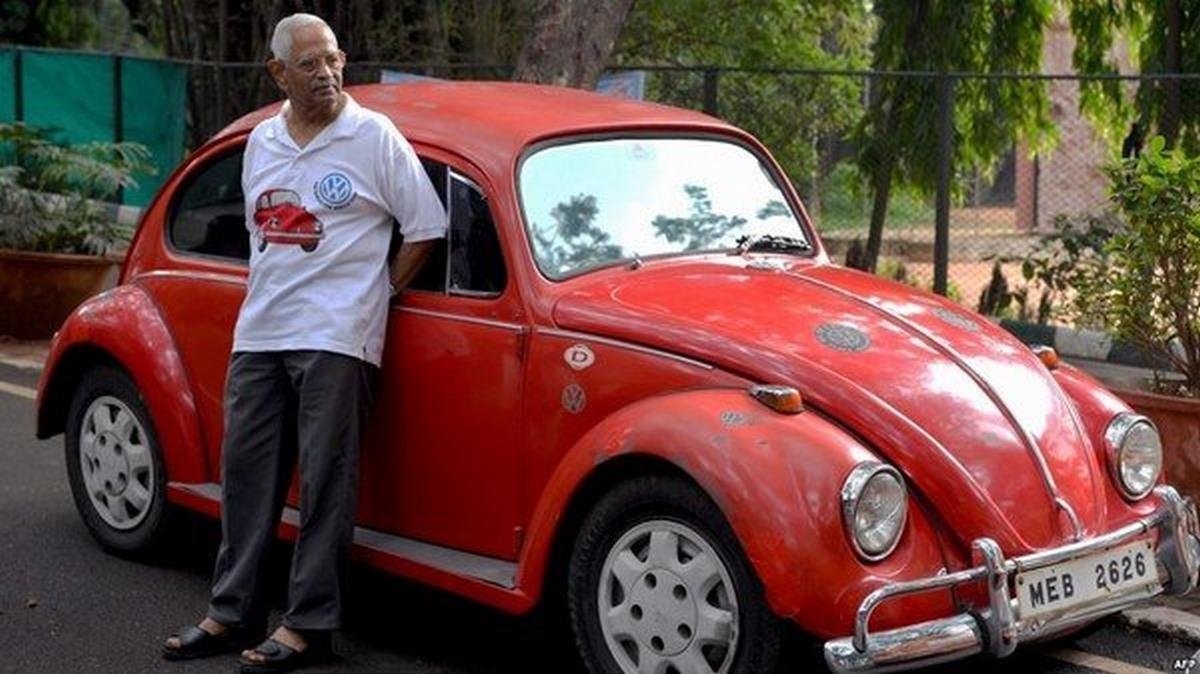 a man next to Volkswagen Beetle red color